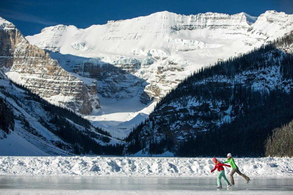 two people ice skate on a frozen lake in Banff