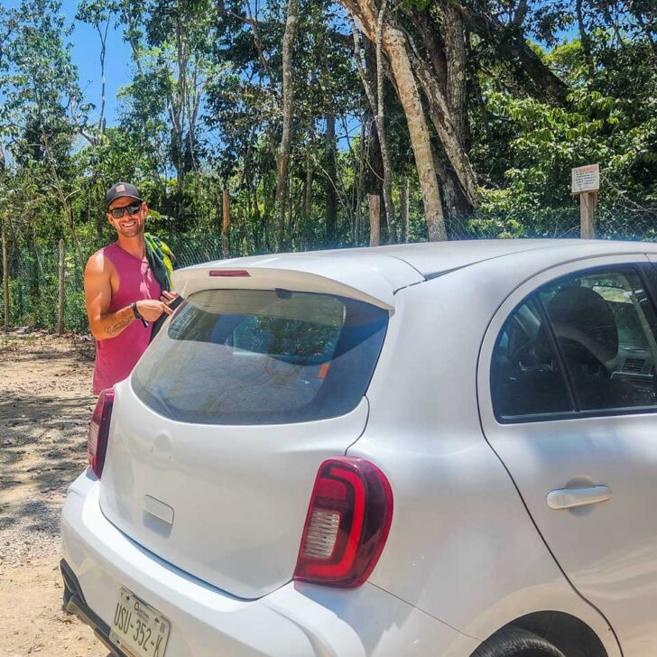 Daniel poses for a photo with our rental car at a cenote in tulum, Mexico
