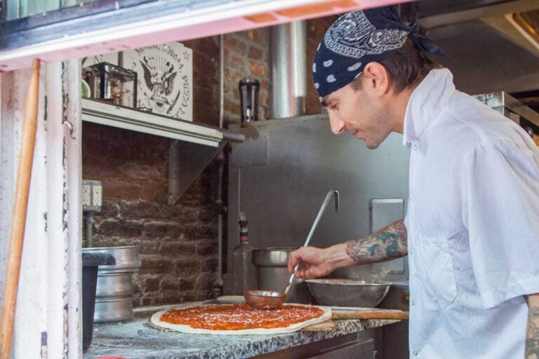 A chef puts sauce on a pizza in Little Ital in NYC on a food tour