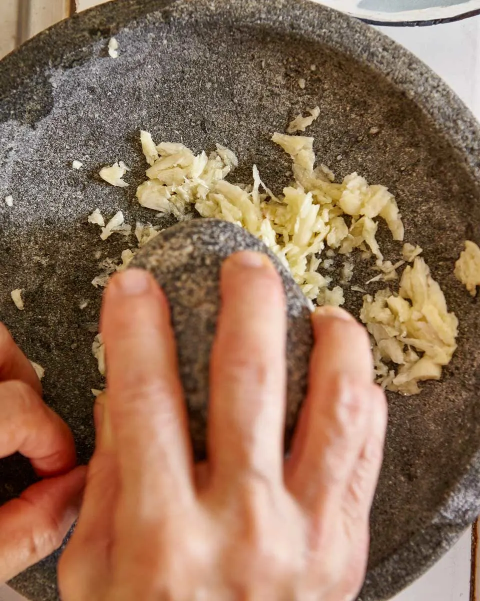 A person grinds up garlic in a stone bowl making pesto during a cooking class in Genoa Italy