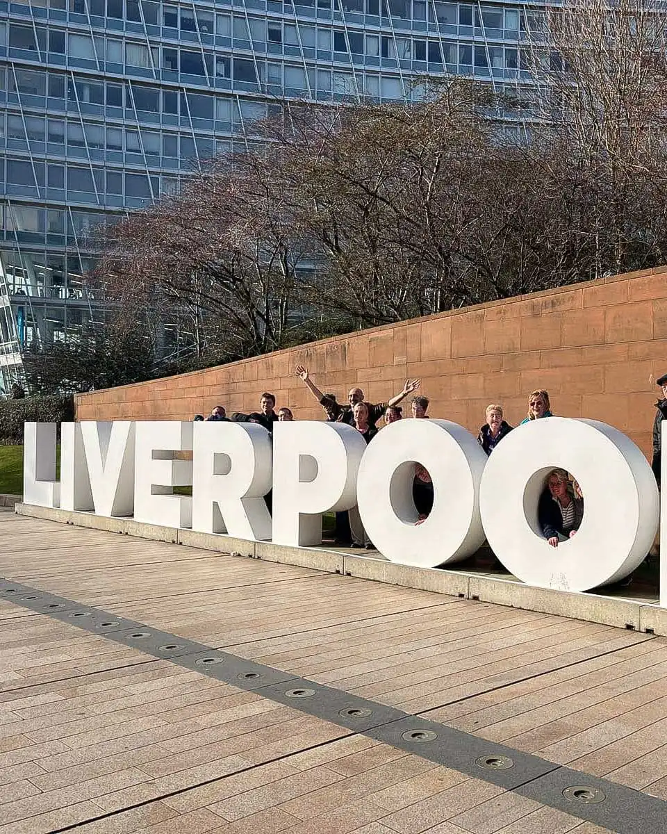 People pose with the Liverpool sign on a walking tour in Liverpool UK