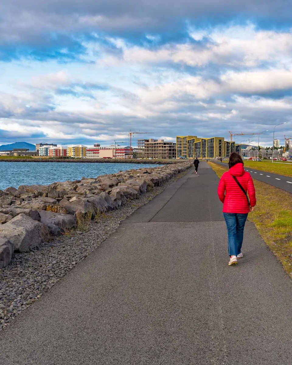 A woman walks along the ocean in Vesturbær Reykjavik Iceland