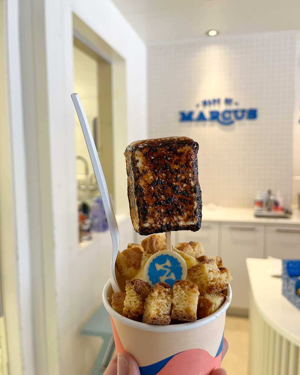 Bailey hold her ice cream up by the Made By Marcus sign in Calgary, Alberta