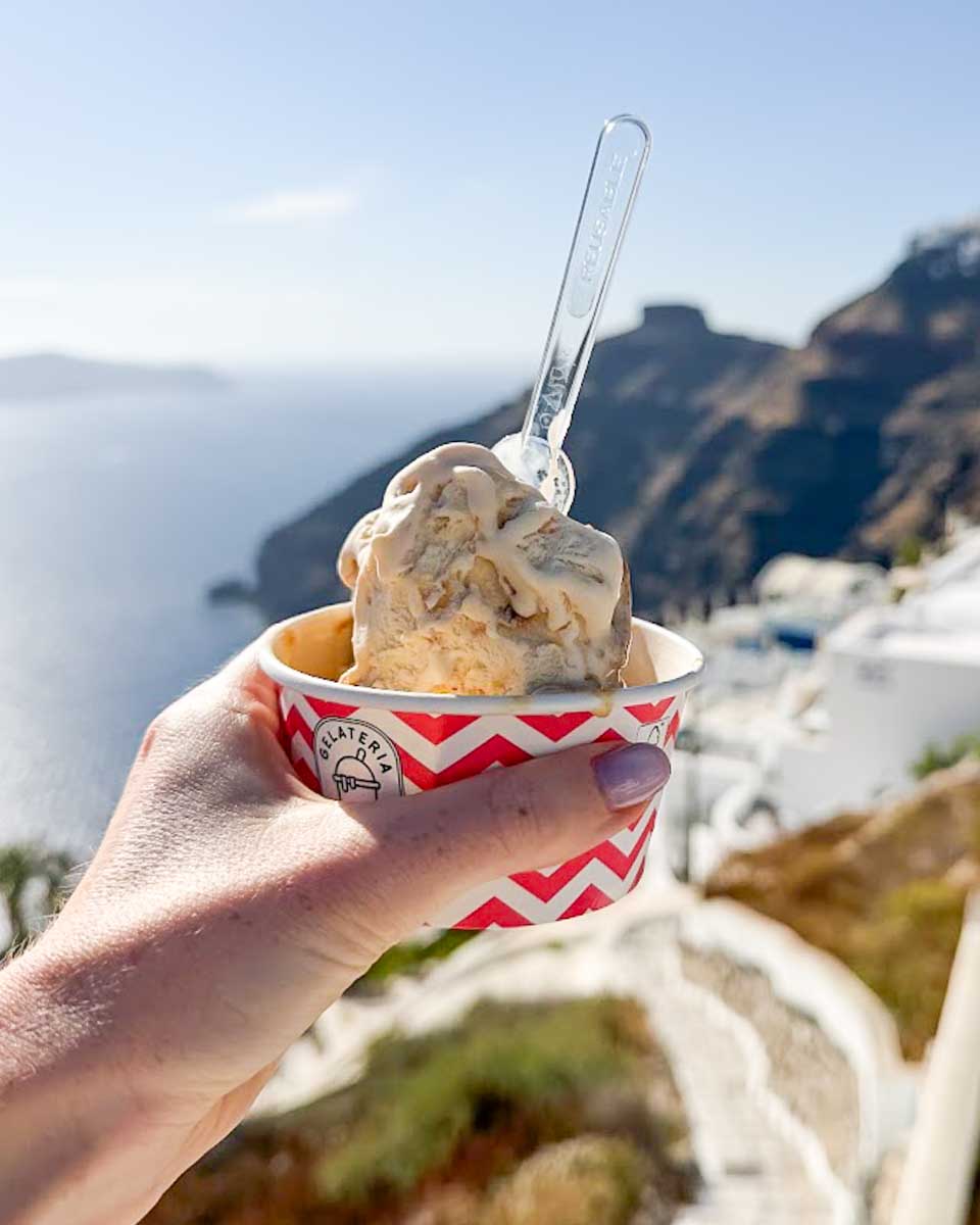Hand holding a cup of gelato overlooking the caldera in Santorini