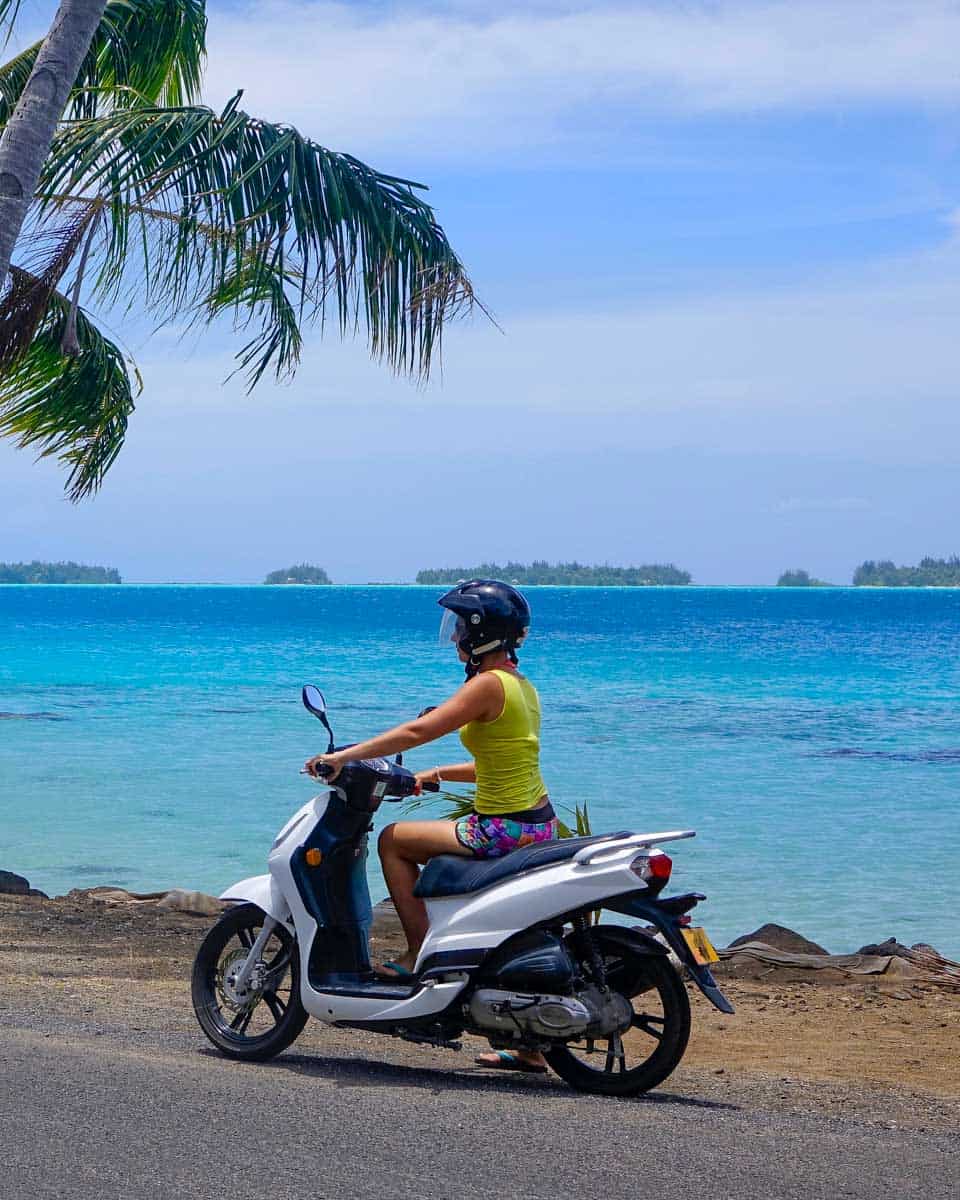 A woman rides a scooter in Bora Bora