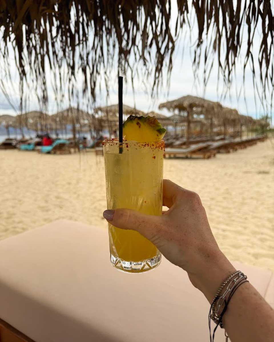 Hannah holding yellow cocktail on the beach in Naxos Greece