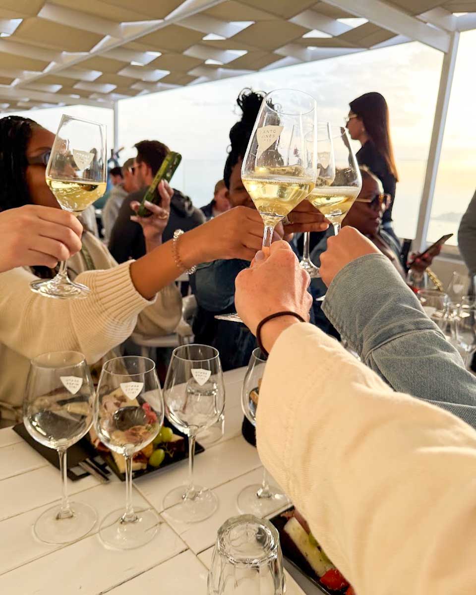 People toasting with glasses of white wine during a sunset wine tasting in Santorini