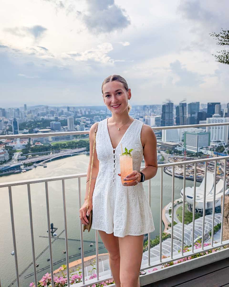 Bailey holding a cocktail with the Singapore skyline behind her