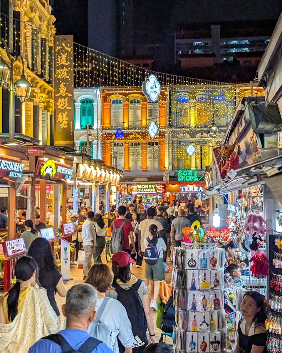 Crowds walking through Chinatown at night in Singapore, with illuminated shophouses and street stalls