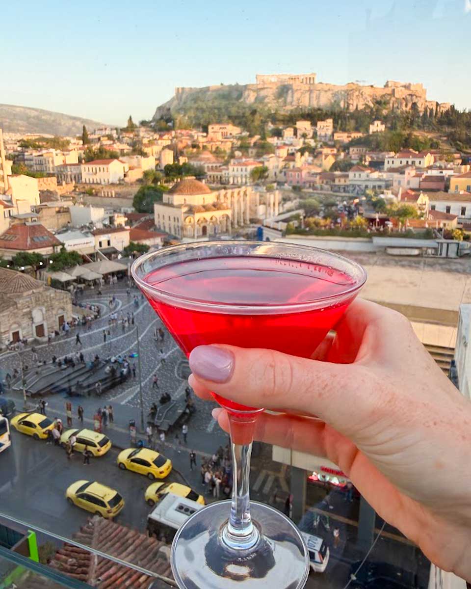 A red cocktail with the Acropolis in the background from a rooftop bar in Athens