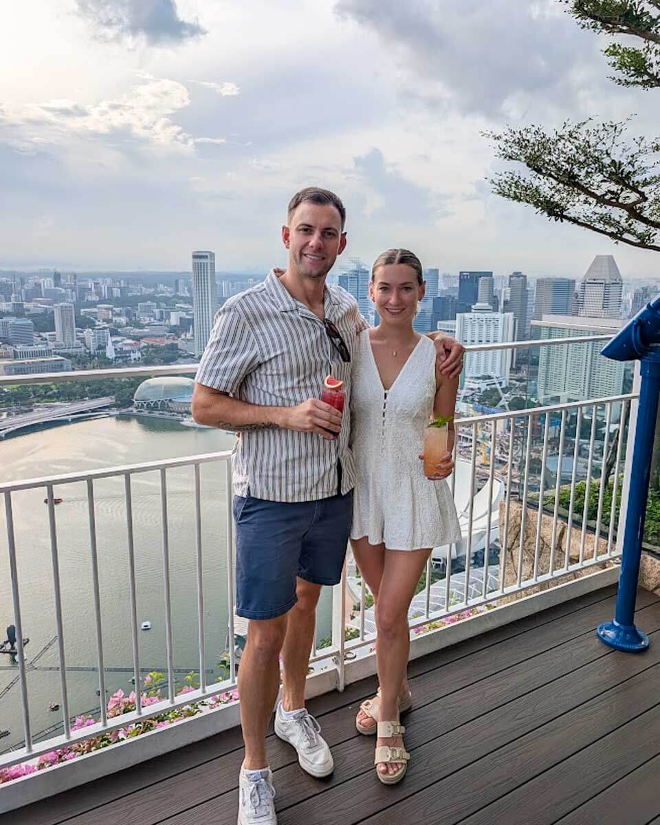 Daniel and Bailey holding cocktails at LAVA Bar with Marina Bay Sands in the background