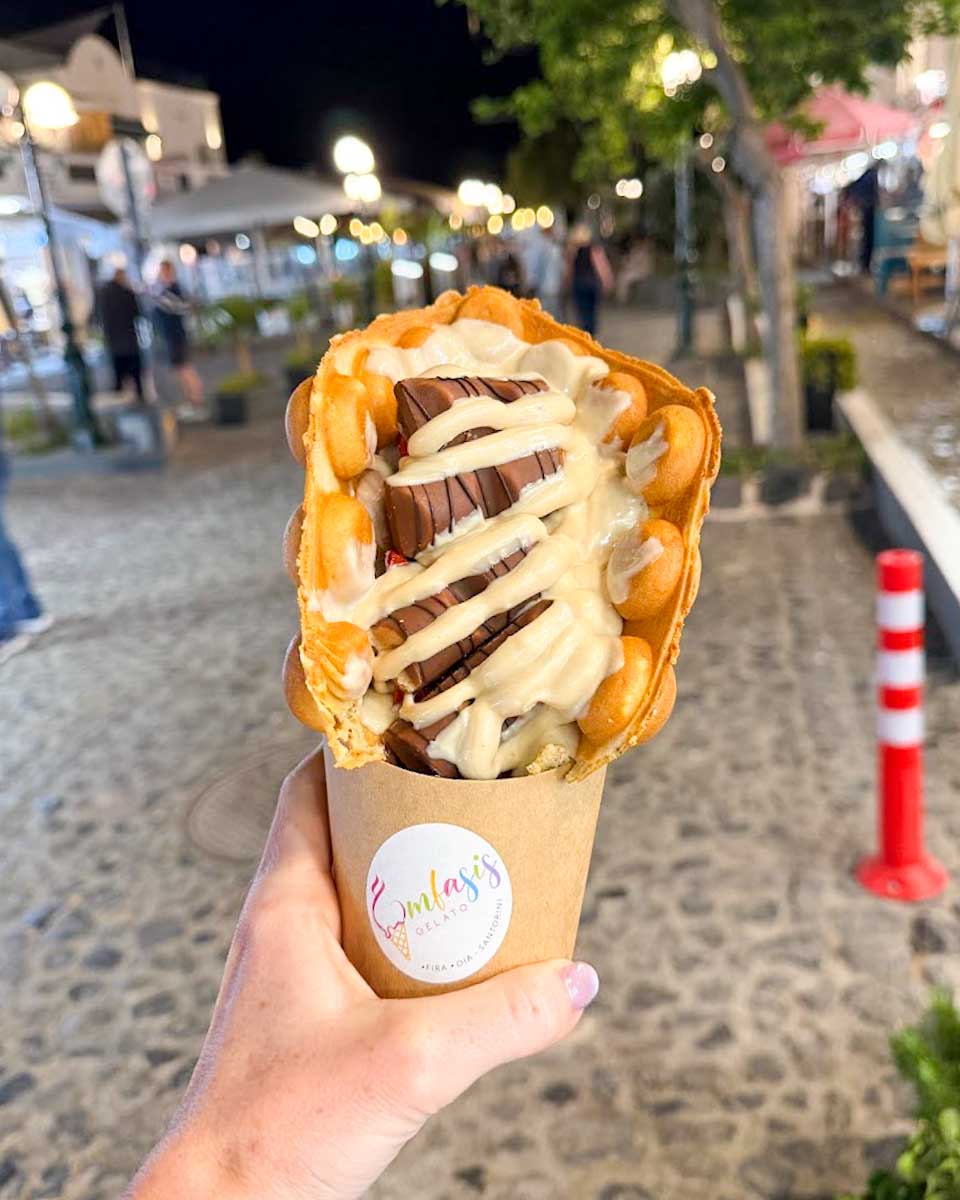 Hannah holding a strawberry and Kinder Bueno waffle at Emfasis in Santorini Greece