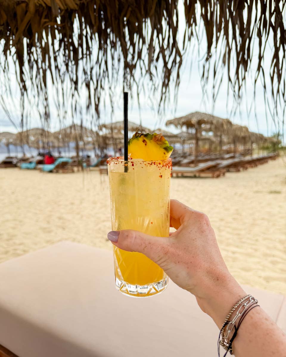Hannah holding yellow cocktail on the beach bar in Plaka, Naxos