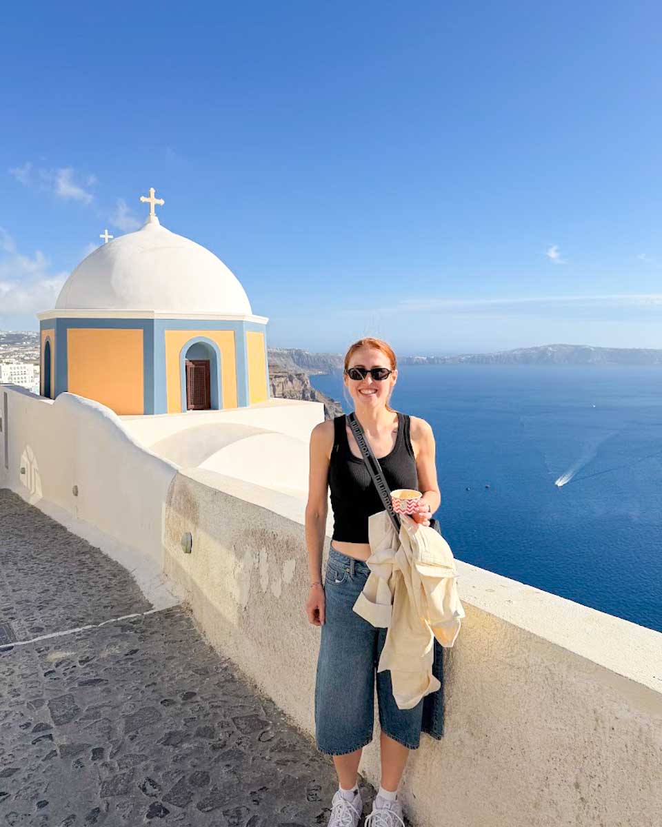 Hannah standing along the Caldera Path with whitewashed buildings in Santorini