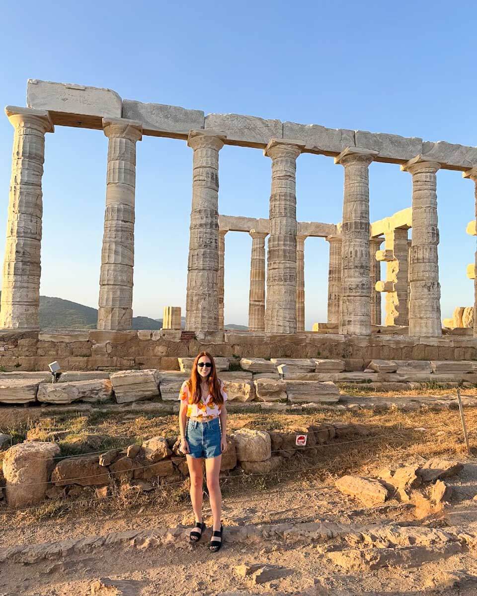 Hannah standing in front of the Temple of Poseidon at Cape Sounion during sunset near Athens, Greece
