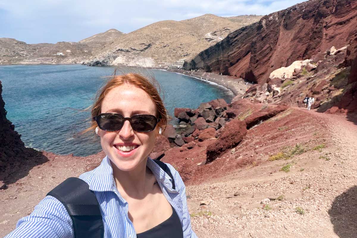 Hannah taking a selfie at Red Beach in Santorini with volcanic cliffs and the Aegean Sea in the background