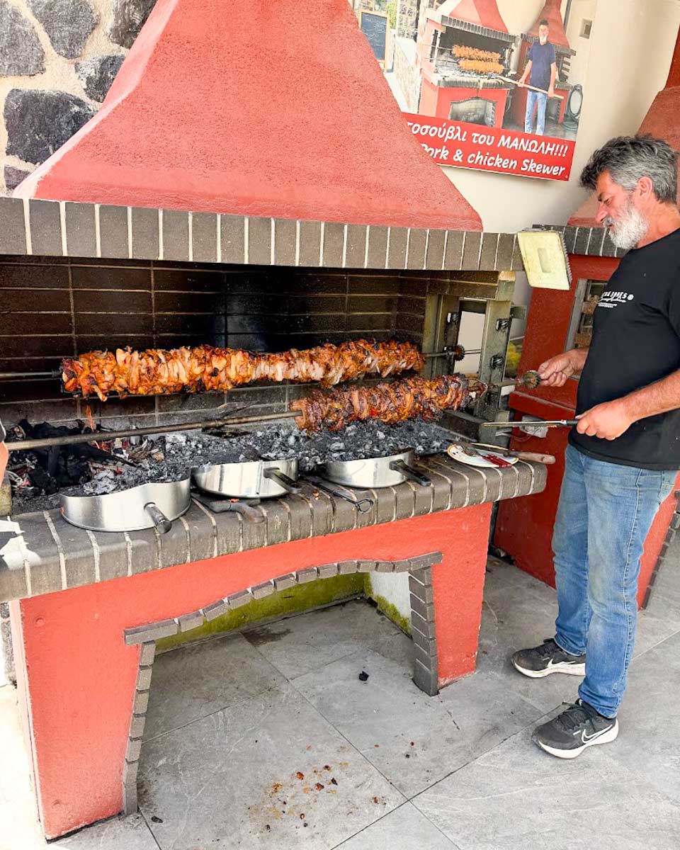 Restaurant owner grilling meat over charcoal at Peirasmos Restaurant near Red Beach in Santorini