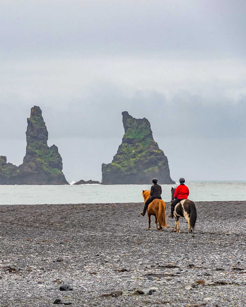 People ride horses on Reynisfjara black sand beach near Vik Iceland 1