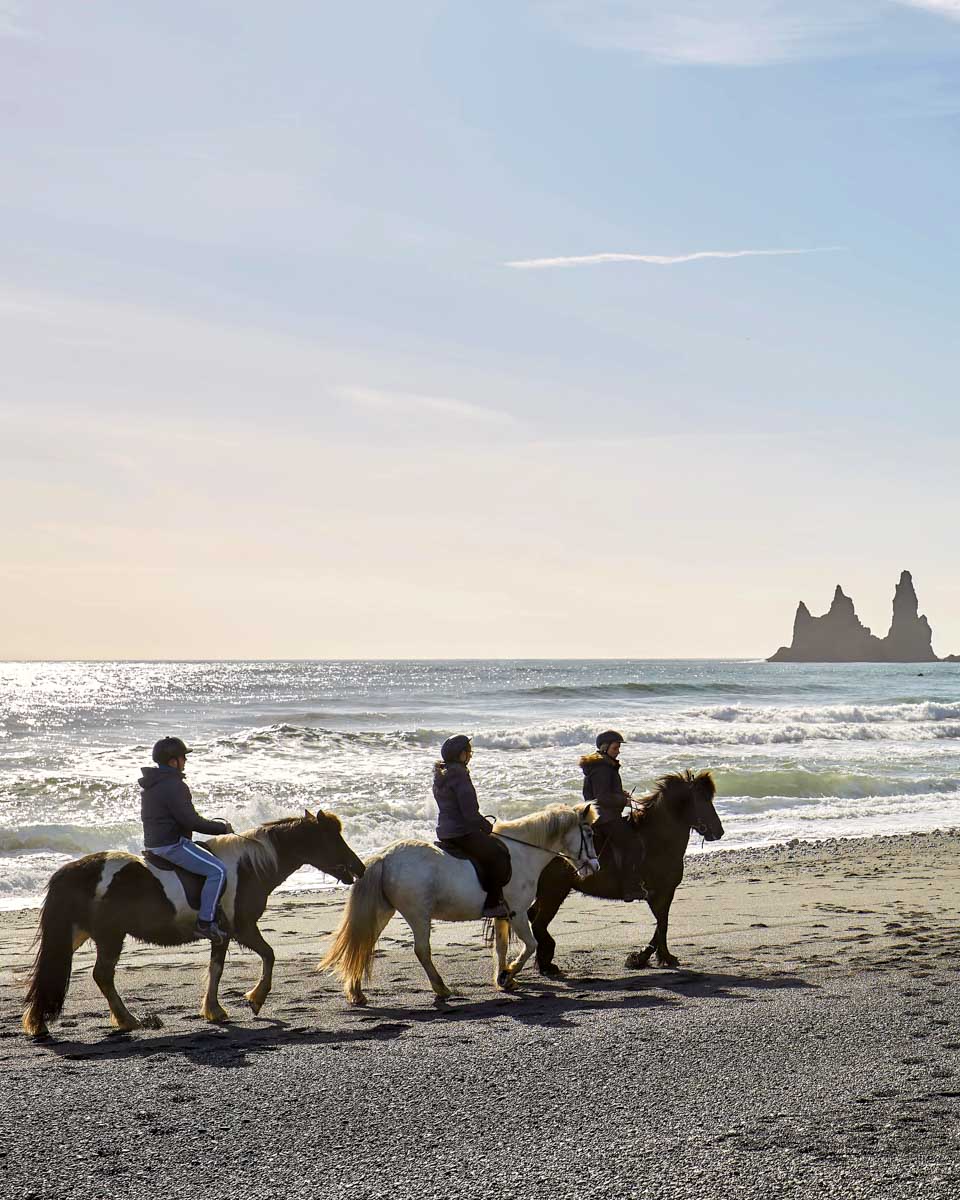 People ride horses on Reynisfjara black sand beach near Vik Iceland