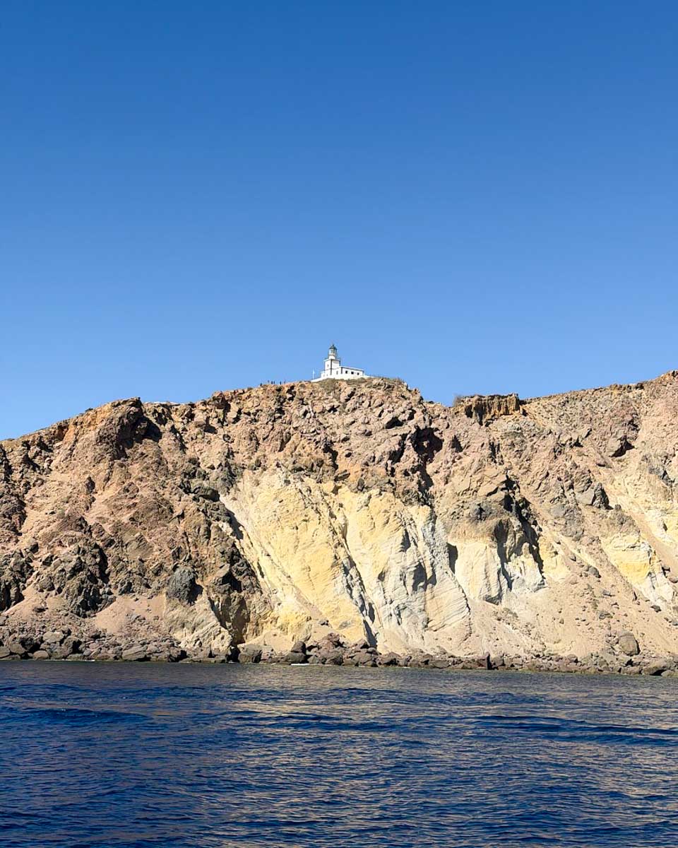 Akrotiri Lighthouse perched on the volcanic cliffs of Santorini, viewed from the sea
