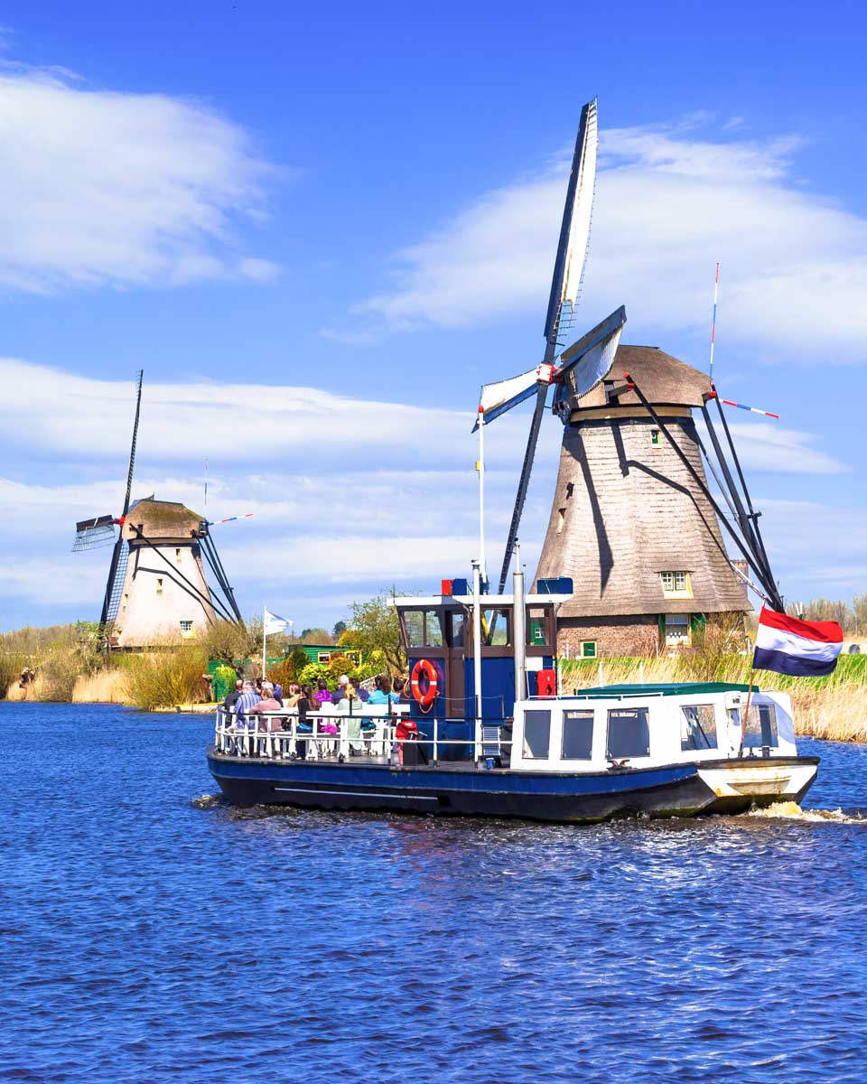 A boat rides down the river in front of a windmill in Kinderdijk Netherlands