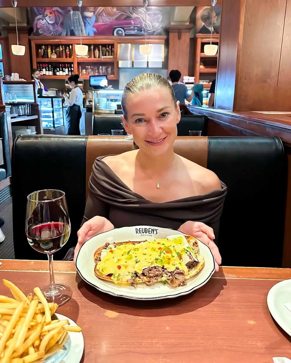 Bailey posing for a photo with open face meat sandwich in plate at Reuben's Deli and Steakhouse Montreal