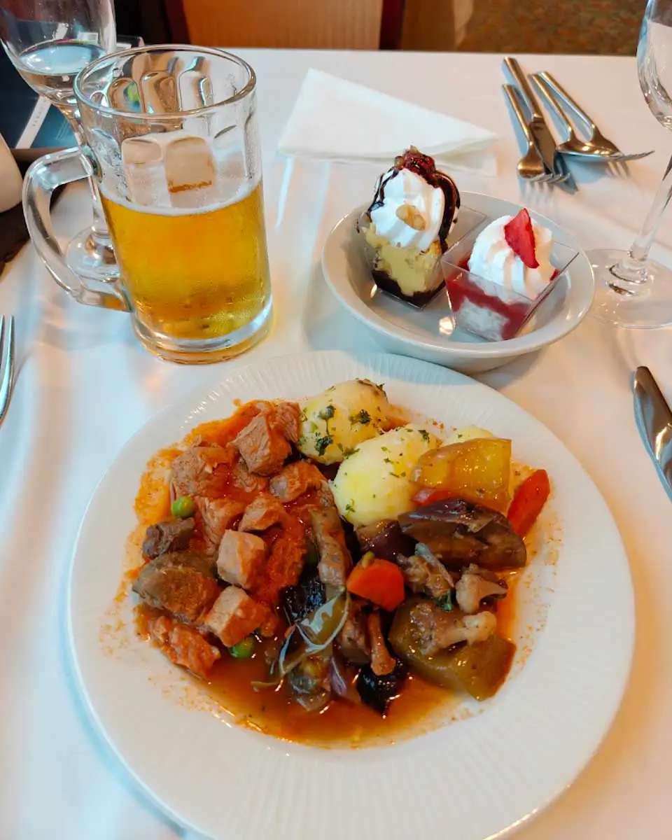 Buffet dinner plate with Hungarian dishes, dessert, and beer served on a Danube River cruise in Budapest