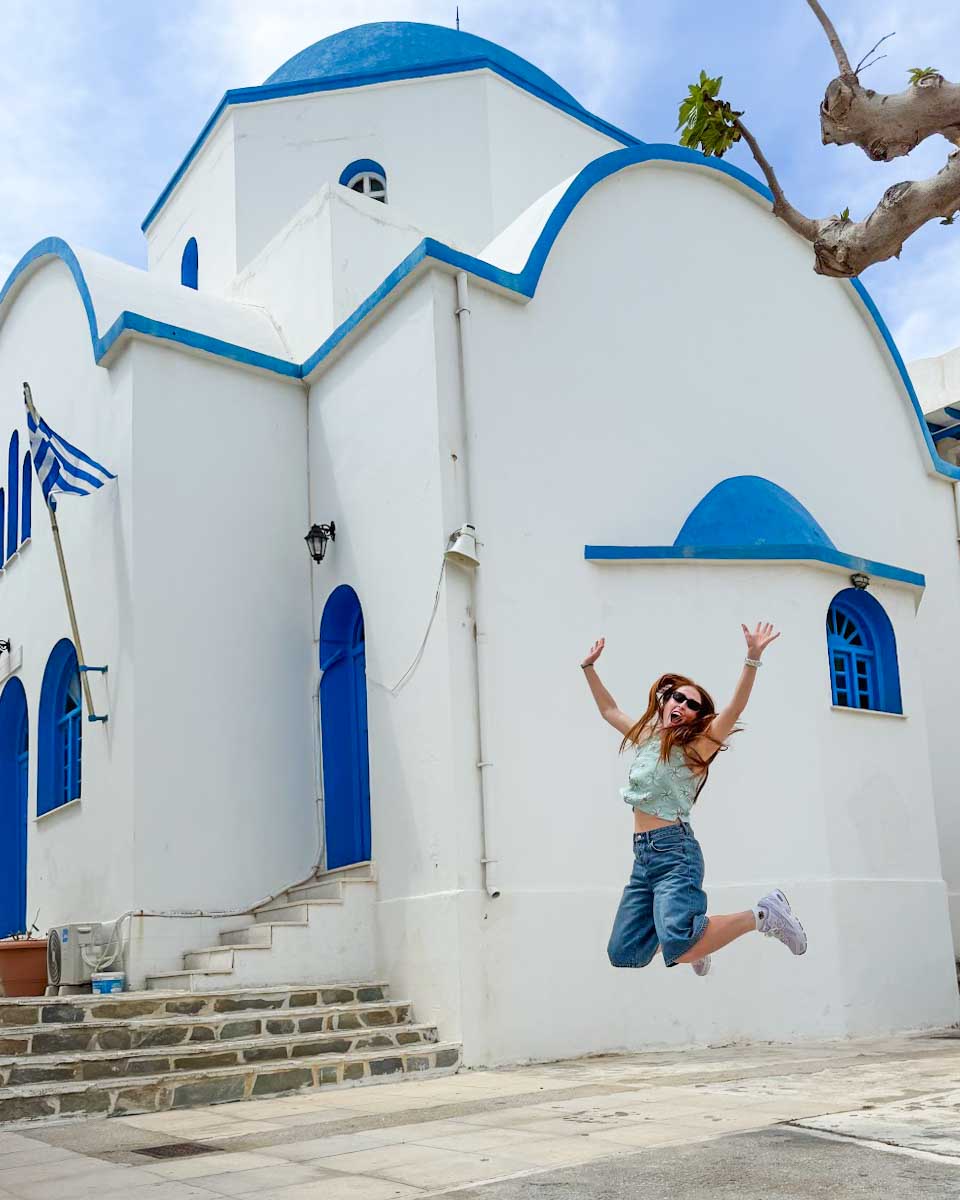 Hannah jumps in front of a white and blue building in Naxos Greece