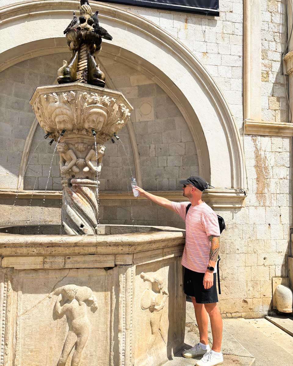 Jesse filling up his water bottle directly from a historic fountain in Old Town Dubrovnik