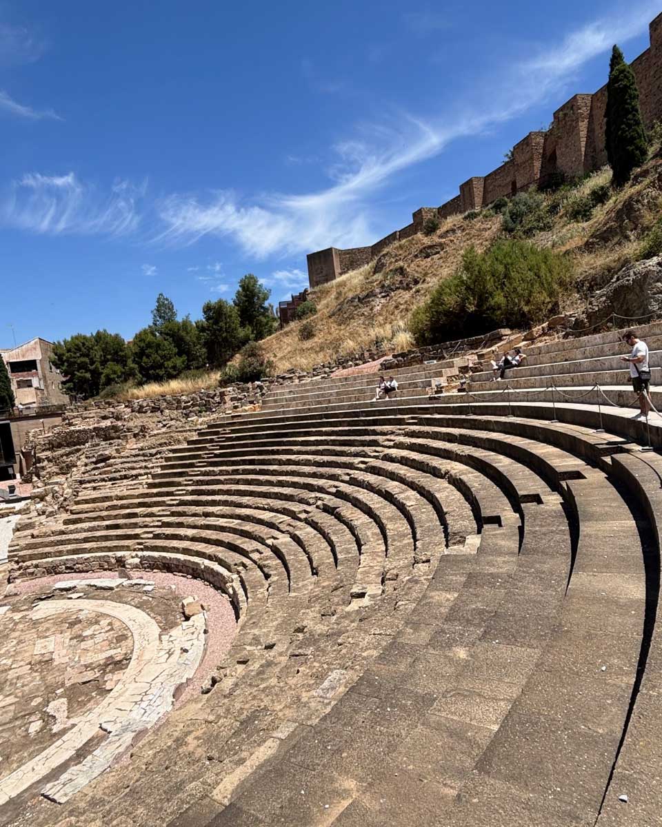 People sit on the steps of the Roman Theatre in Malaga, Spain