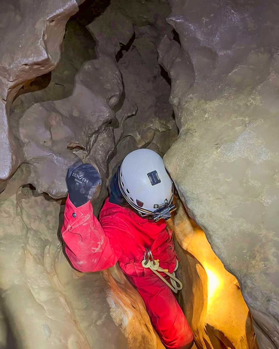 Person squeezes through a gap in the cave on a tour with Canmore Cave Tours