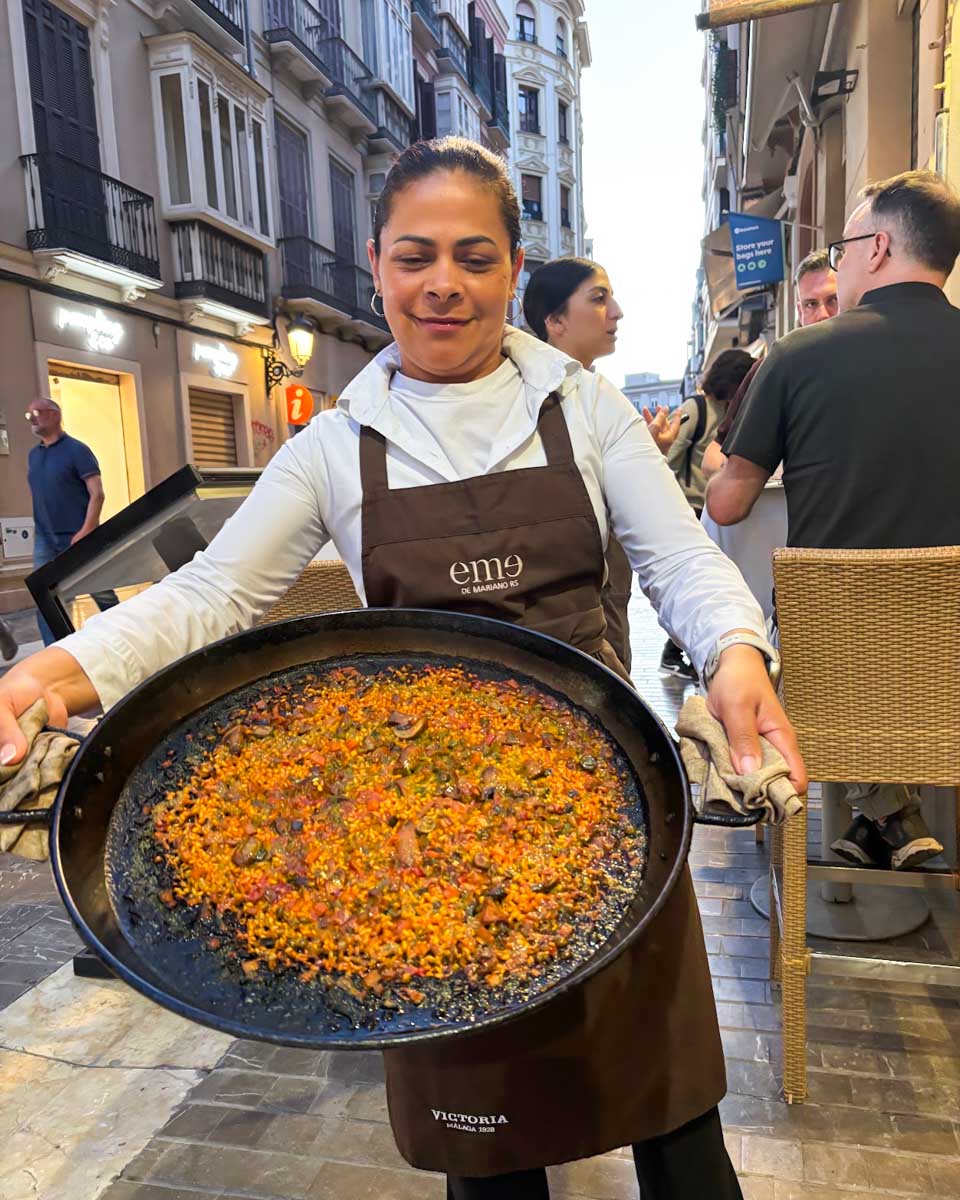 A woman holds up a pan of paella on a food tour in Malaga