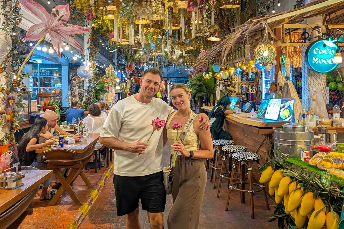 Bailey and Daniel smile in a market holding lotus flowers in Thailand