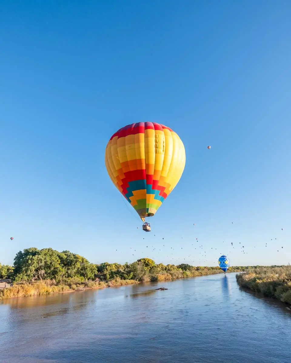 A vibrant multicolor hot air balloon flies low over the Rio Grande River, Albuquerque, New Mexico