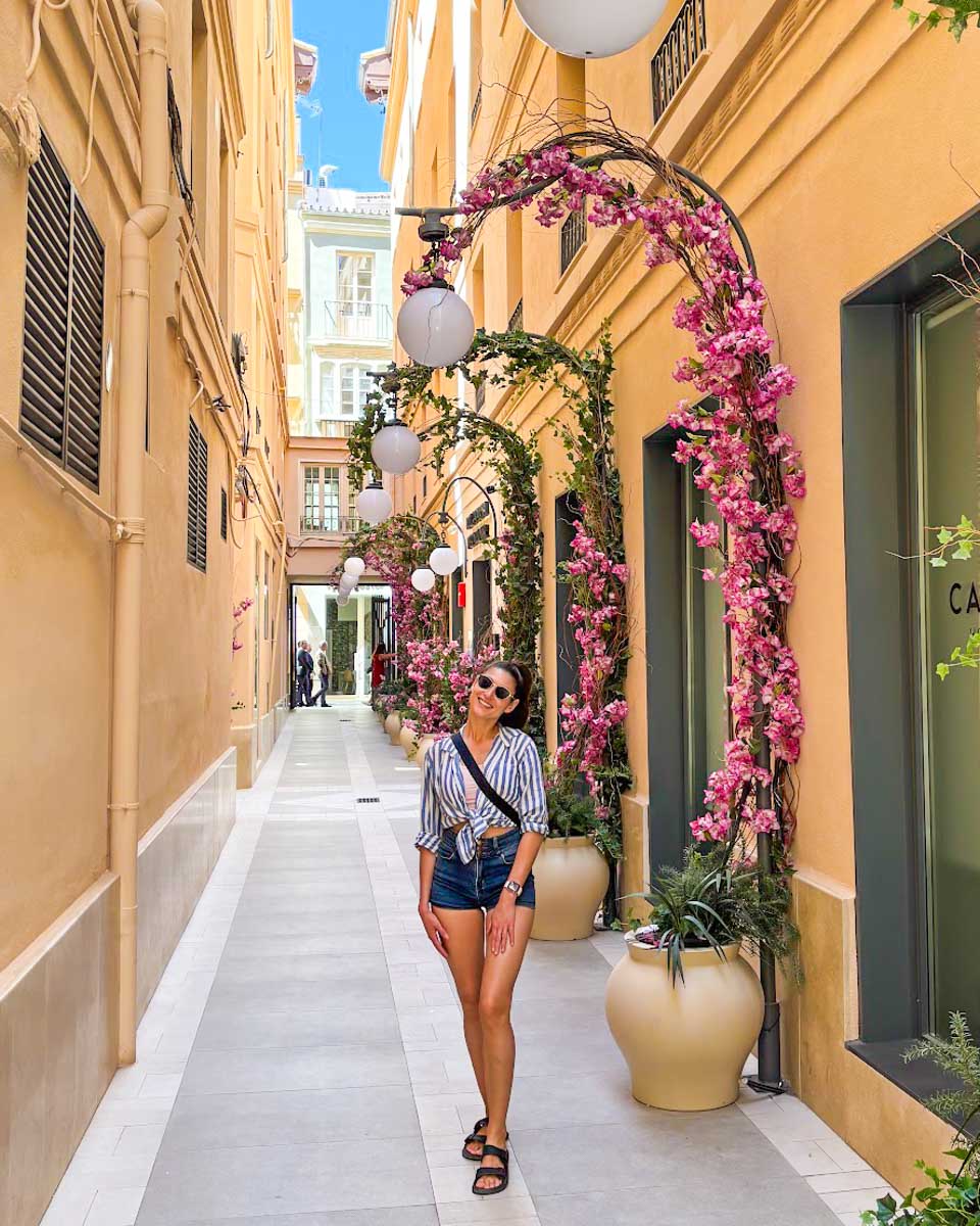 Brittni poses on a street with pink flowers in Malaga, Spain