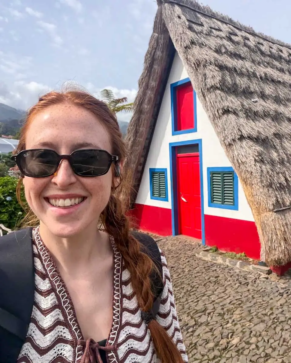 Hannah taking photo with A-frame cottage in background in Santana, Madeira Portugal